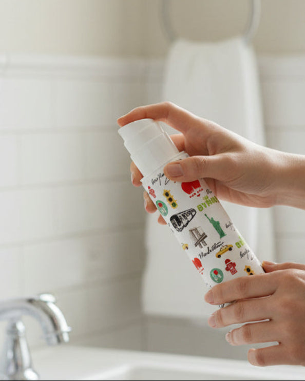 Person holding a bottle of sunscreen in front of a bathroom sink.