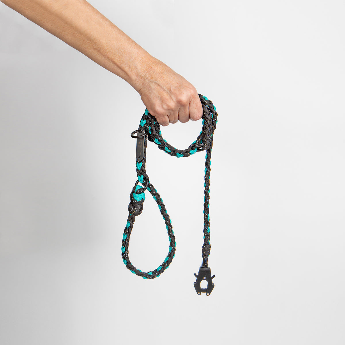 Hand holding a braided dog leash with black and teal pattern on a light gray background