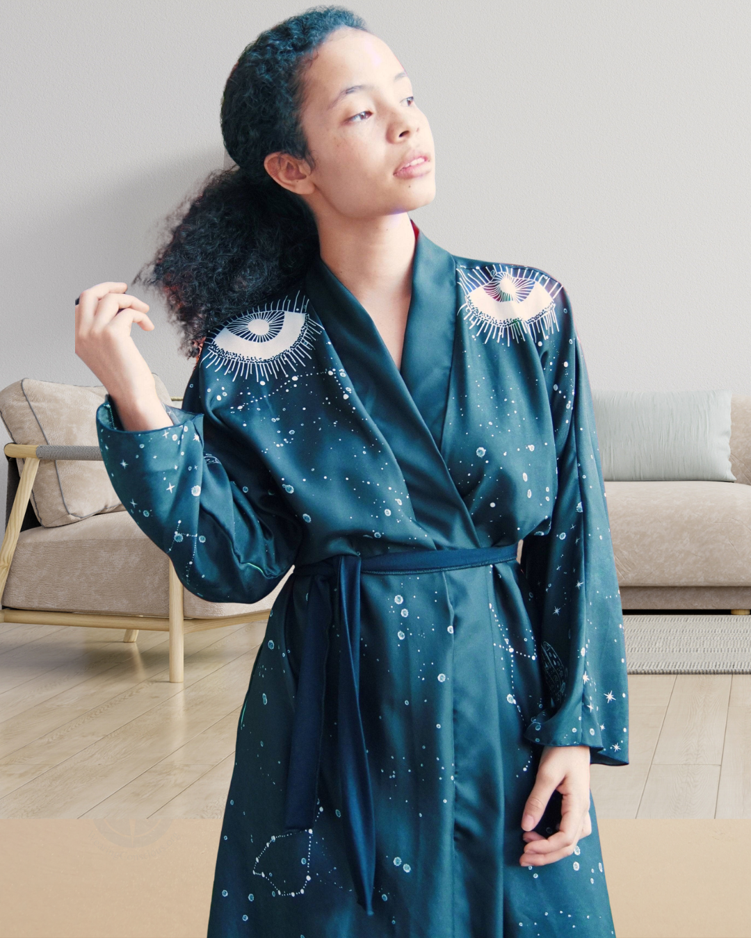 Woman wearing a teal robe with celestial designs in a living room.