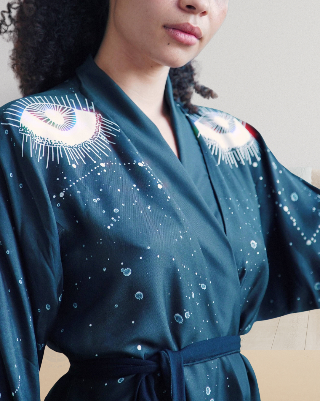 Person wearing a teal robe with white eye designs and star patterns.