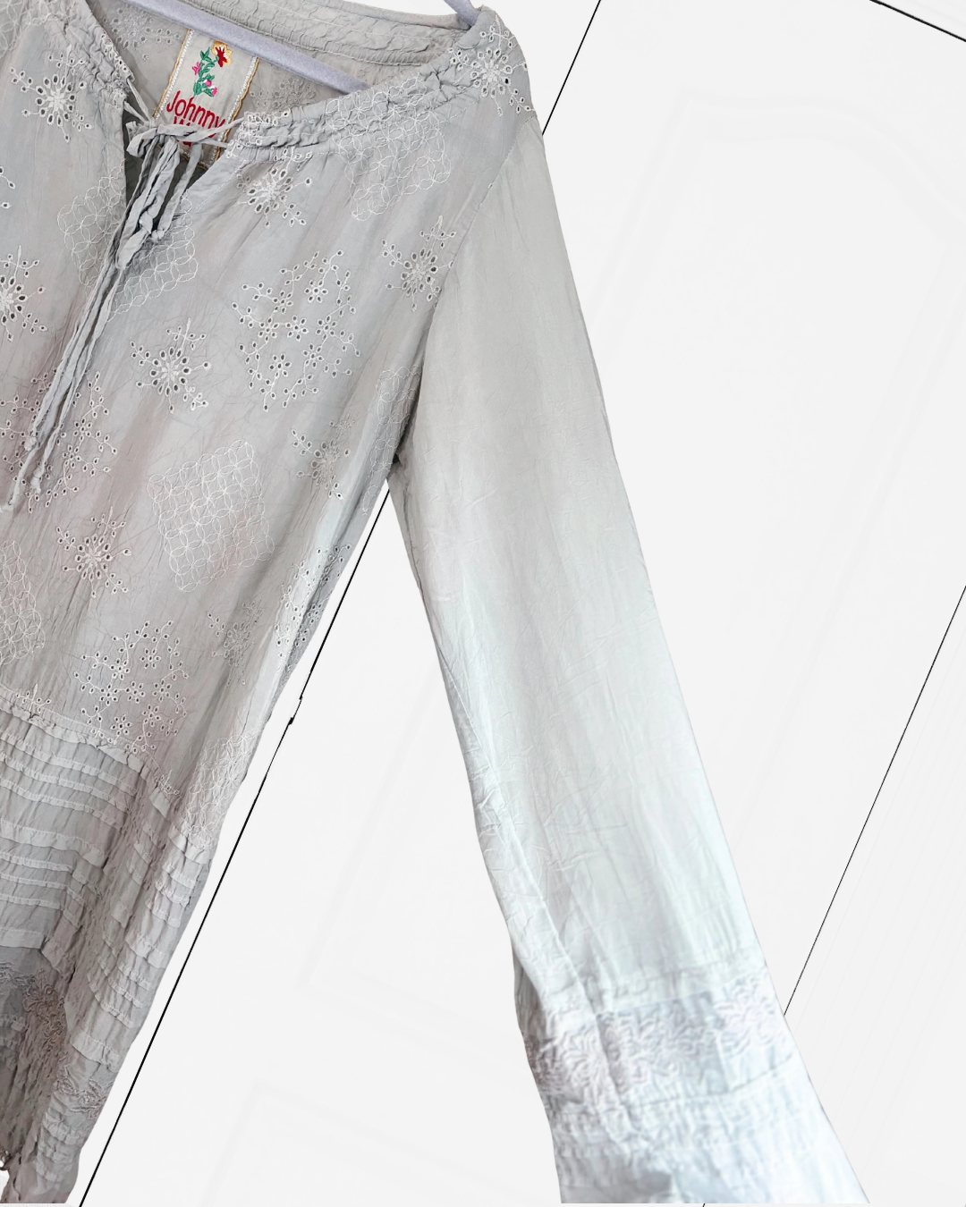 Gray eyelet embroidered cupra rayon long-sleeve blouse with a tie-neck detail, shown hanging on a white hanger against a white paneled background