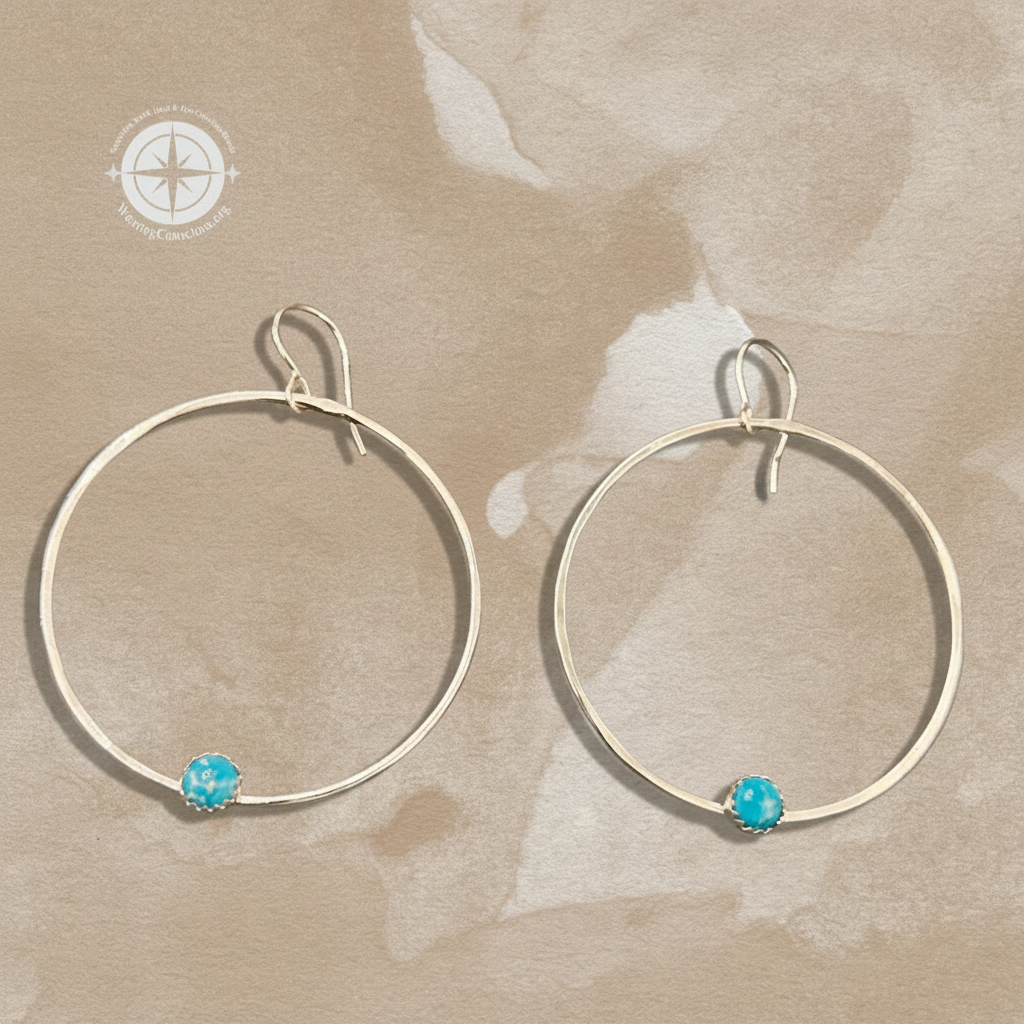 A pair of large silver-tone hoop earrings with a small round turquoise-blue stone at the bottom of each hoop, displayed on a textured beige background.