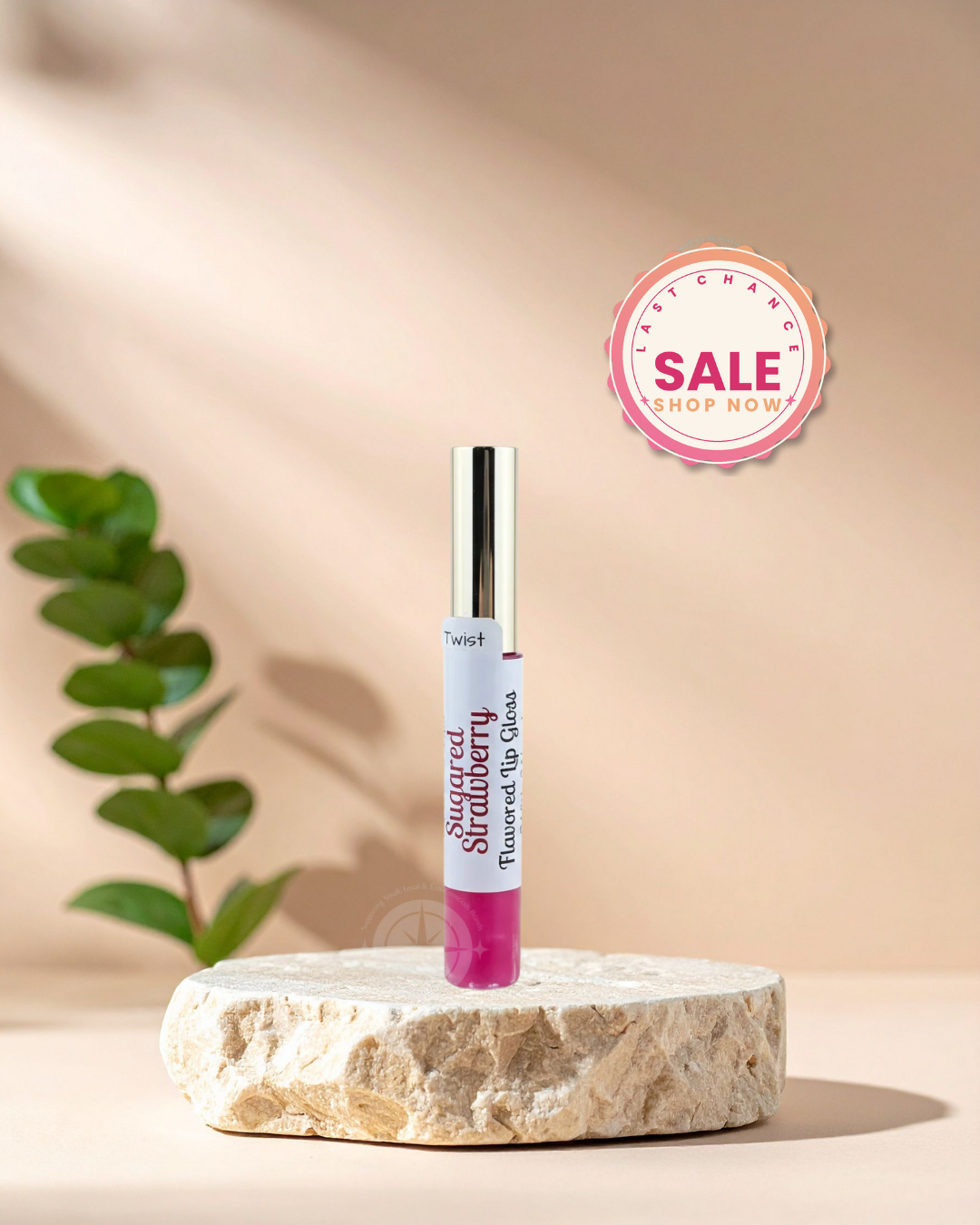 A tube of Tweezlip Strawberry Flavored Lip Gloss stands upright on a round stone pedestal against a warm beige background with soft shadows and a green plant leaf on the left. A pink circular 'Fast Change Sale Shop Now' badge appears in the upper right.