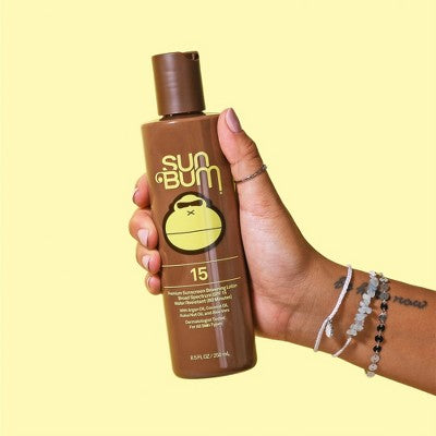 Hand holding a bottle of Sun Bum sunscreen lotion against a yellow background