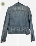 A blue denim jacket hanging on a black hanger against a white background, featuring the names 'VAL' and 'FLEURY' spelled out in rhinestones across the back.
