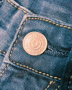 A close-up of a copper-colored metal button on a pair of blue denim jeans, showing the brand name 'FREDERICK JENNING' and the 'F' logo.