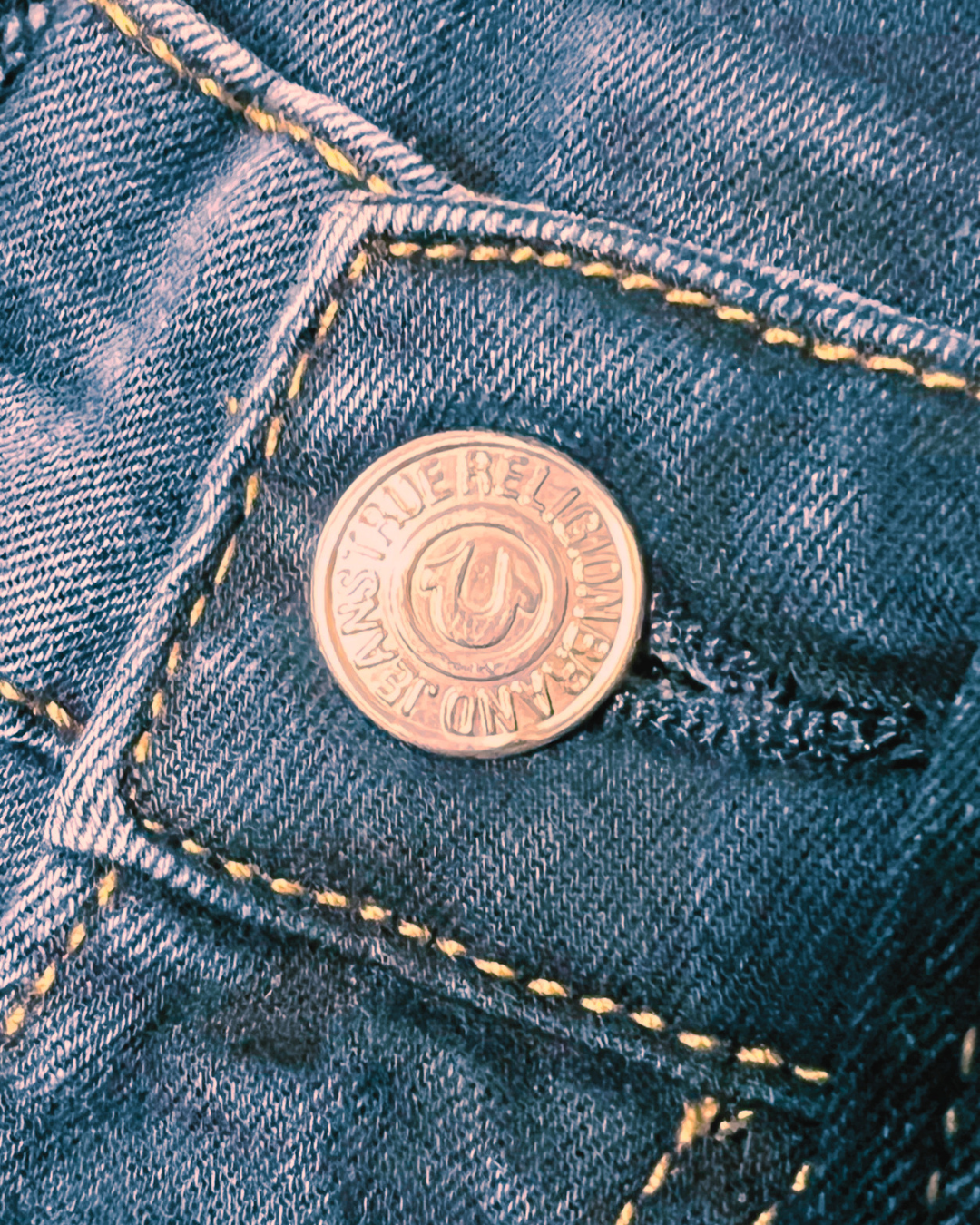 A close-up of a copper-colored metal button on a pair of blue denim jeans, showing the brand name 'FREDERICK JENNING' and the 'F' logo.