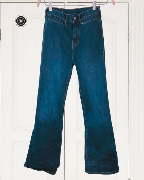 A pair of dark blue flare jeans hanging on pink hangers against a white paneled door background.