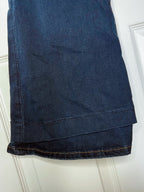 A close-up of a dark blue denim garment, likely jeans or trousers, folded over a white paneled door. The fabric shows a classic indigo wash with visible orange-tan contrast stitching along the hem.