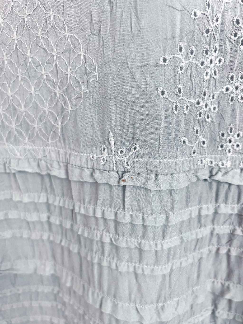 Close-up of a light gray fabric garment featuring white embroidered floral patterns and ruffled tiers.