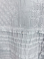 Close-up of a light gray fabric garment featuring white embroidered floral patterns and ruffled tiers.