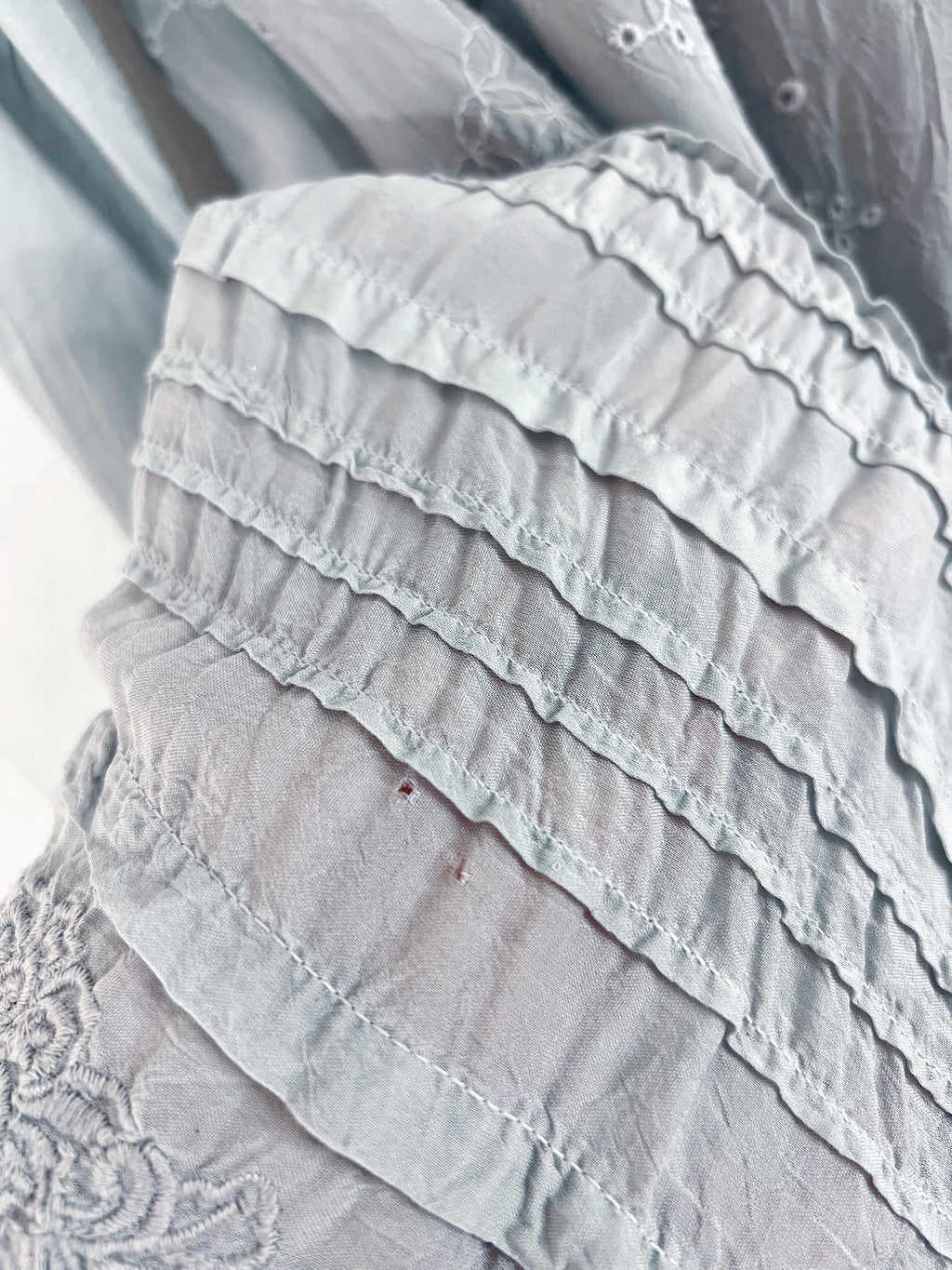 Close-up of a light gray ruffled fabric garment with layered ruffles and delicate embroidery.