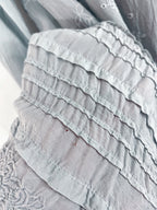 Close-up of a light gray ruffled fabric garment with layered ruffles and delicate embroidery.