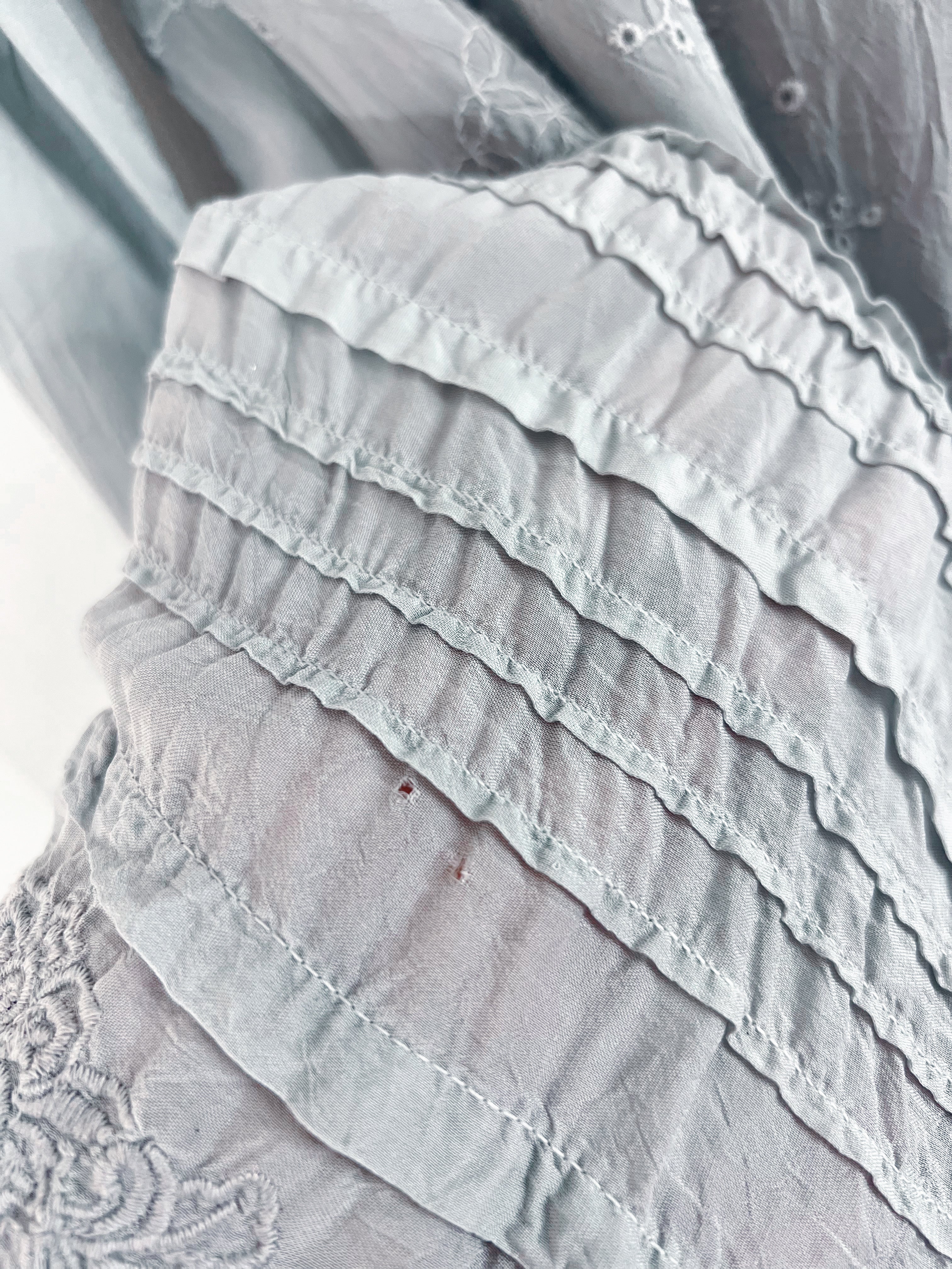Close-up of a light gray ruffled fabric garment with layered ruffles and delicate embroidery.