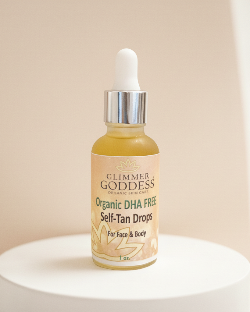 A 1 oz glass bottle of Glimmer Goddess Organic Body Paint Self-Tan Drops with a white dropper cap, displayed on a white cylindrical pedestal against a warm beige background.
