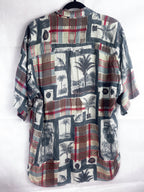 A short-sleeve button-up shirt with a patchwork print featuring plaid patterns, palm tree illustrations, and black-and-white tropical scenes on a white background.