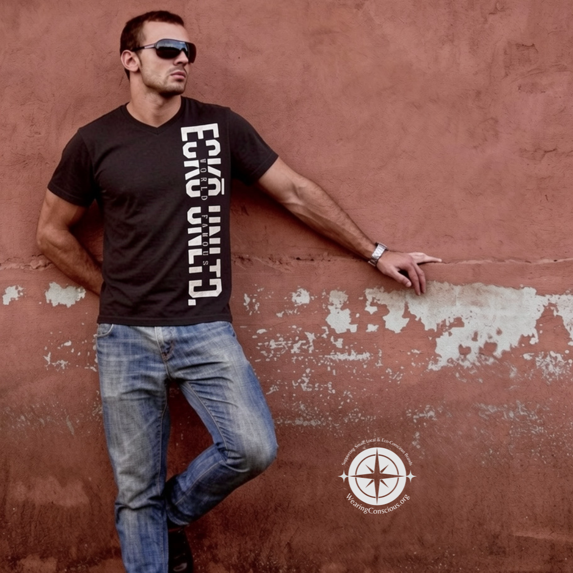 A man wearing a black graphic t-shirt with 'ECO WILD' printed vertically in white, paired with blue jeans, posing against a textured terracotta wall.
