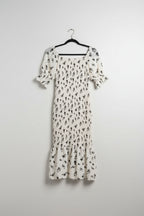 White dress with black floral pattern hanging on a wooden fence with greenery in the background