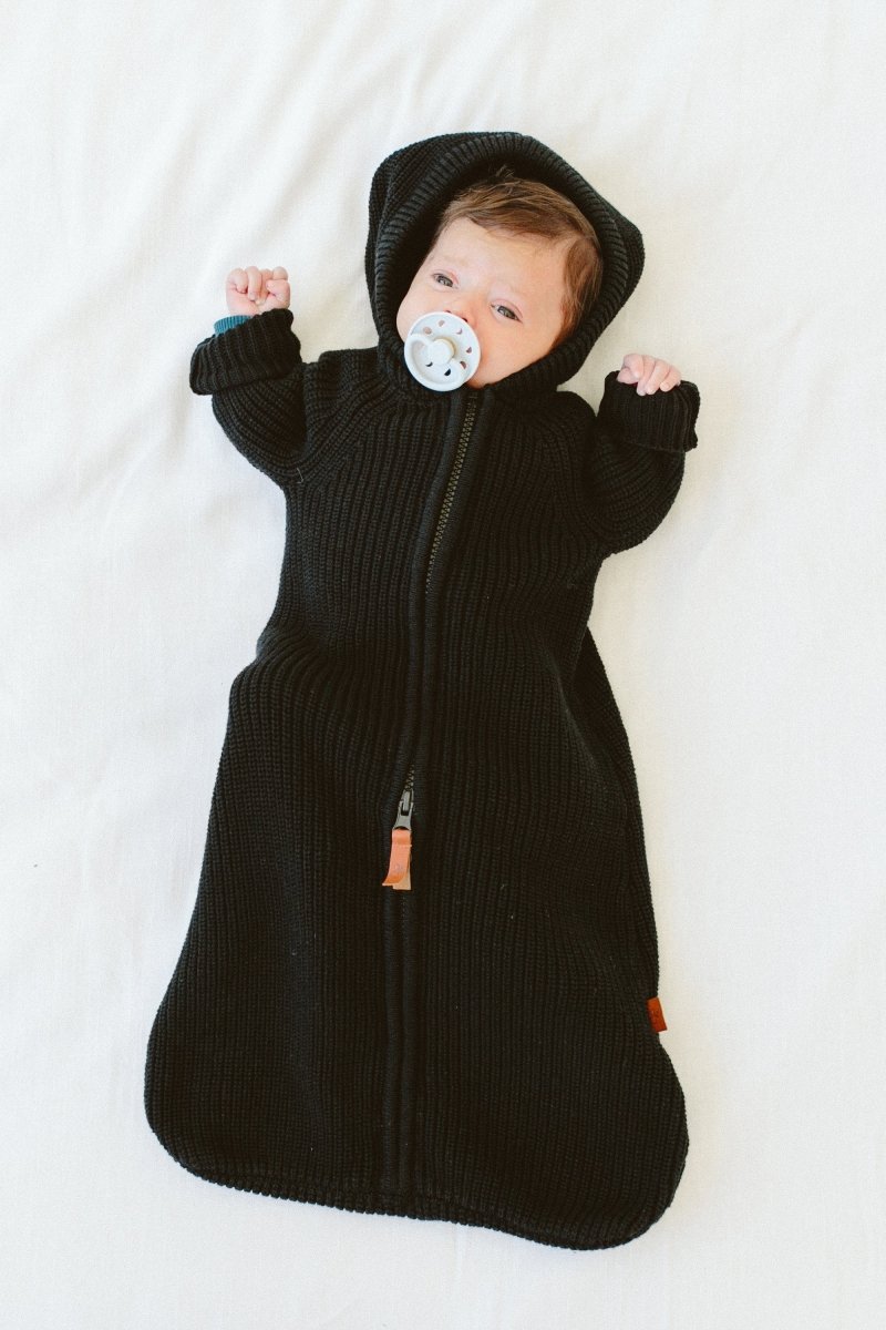 Baby in a black knitted baby bag with a pacifier on a white background