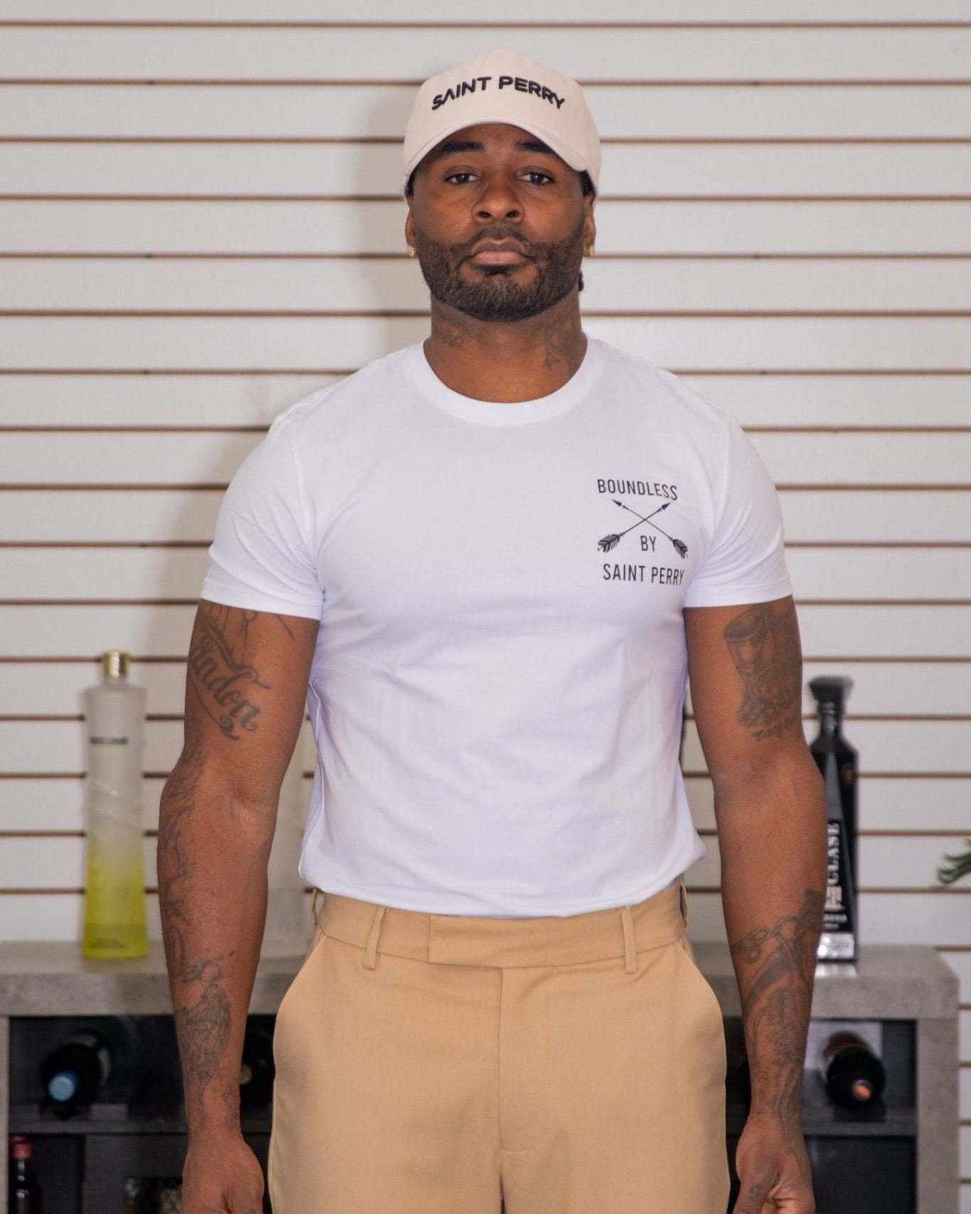 Man wearing a white t-shirt with text and a logo, standing in front of a white wall.