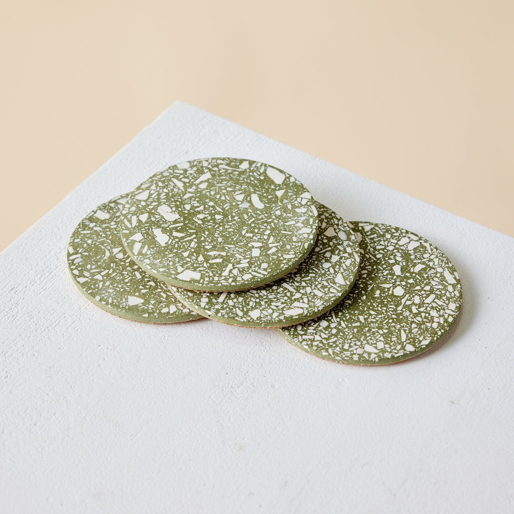 Set of green terrazzo coasters on a white surface with a beige background