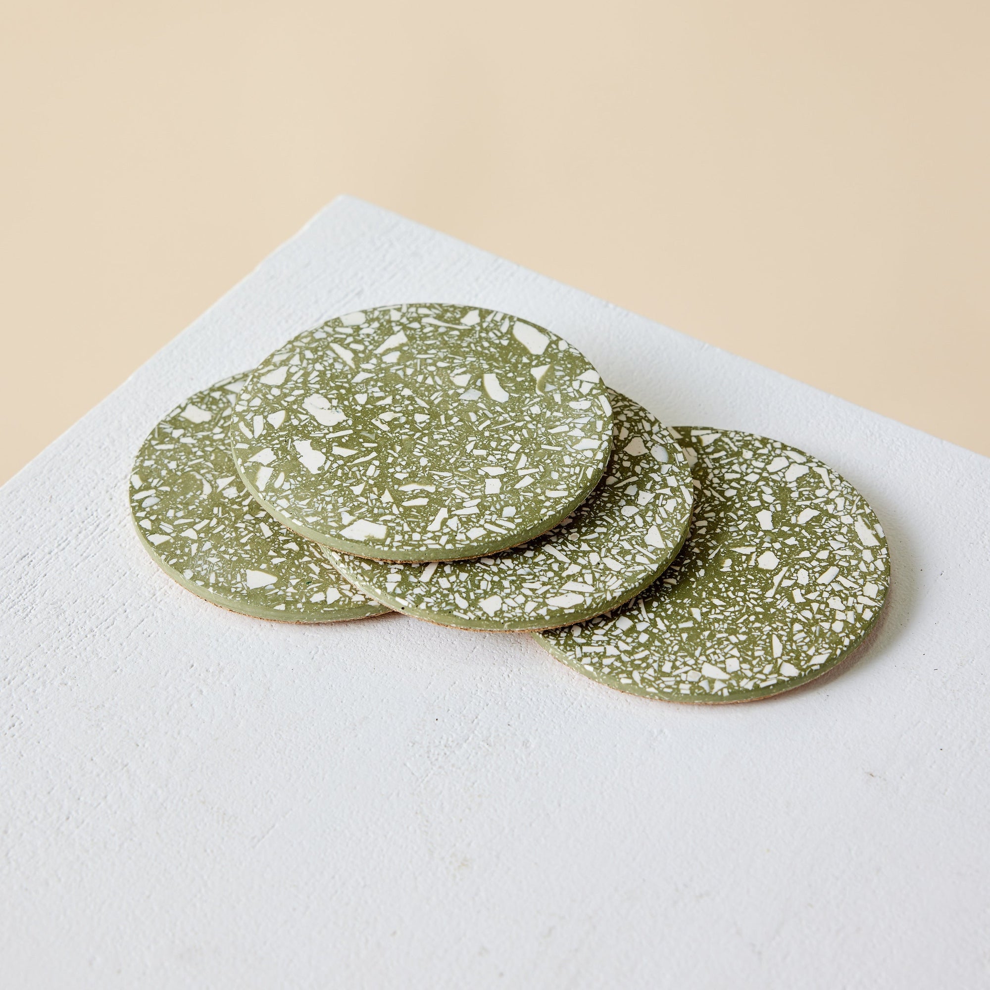Set of green terrazzo coasters on a white surface with a beige background