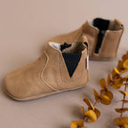 Pair of beige baby shoes on a neutral background with yellow leaves.